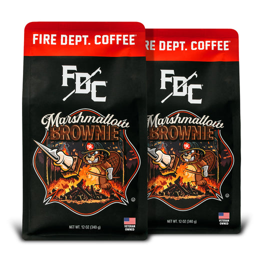 Two bags of Fire Department Coffee’s 12 oz Marshmallow Brownie Coffee with a red section accross the top that says ”Fire Dept. Coffee”. The art on the bag features a beaver holding a pike pole with a marshmallow and brownie on it over a campfire. The title reads, ”Marshmallow Brownie” and there is a veteran owned badge with an American flag in the bottom right corner.