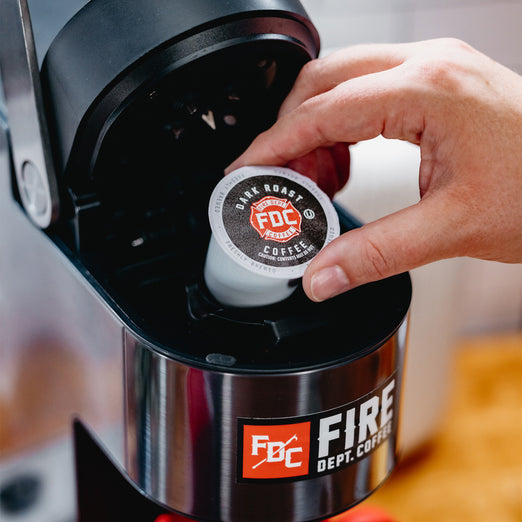 Someone putting a Dark Roast Coffee pod in a brewing machine.