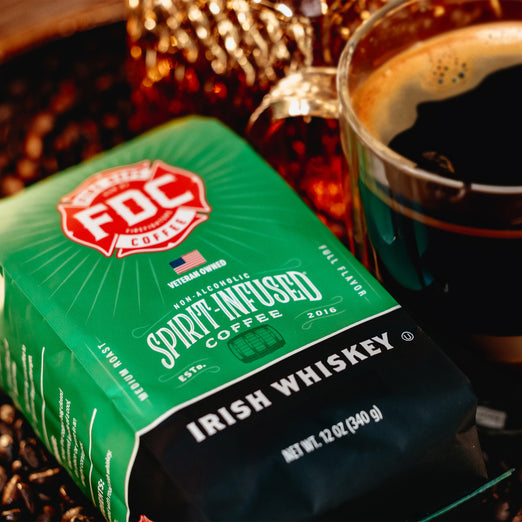 A bag of Irish Whiskey Infused Coffee sitting among coffee beans and a cup of coffee