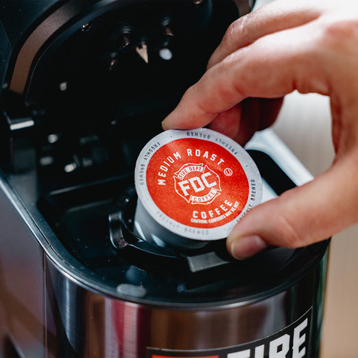 Someone placing an Original Medium Roast Coffee Pod into a brewing machine