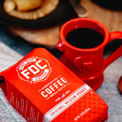 A bag of Original Medium Roast Coffee laying on a table next to a Fire Hydrant Coffee Mug full of coffee