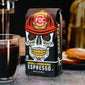 A bag of Skull Crushing Espresso sitting on a table next to a glass of coffee