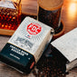 A bag of Vanilla Bean Bourbon Infused Coffee sitting on a table with a bag next to it with coffee beans spilling out