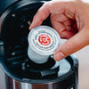Someone placing a Vanilla Bean Bourbon Infused Coffee Pods in a brewing machine