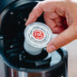 Someone placing a Vanilla Bean Bourbon Infused Coffee Pods in a brewing machine