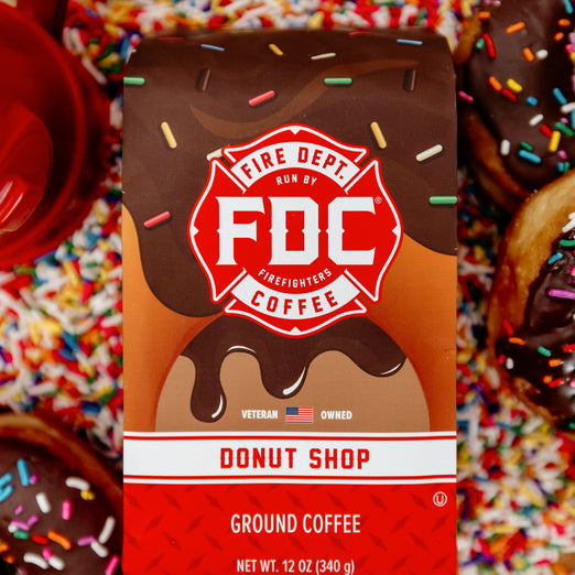 A 12 ounce package of Fire Department Coffee’s Donut Shop Coffee surrounded by rainbow sprinkles and donuts.