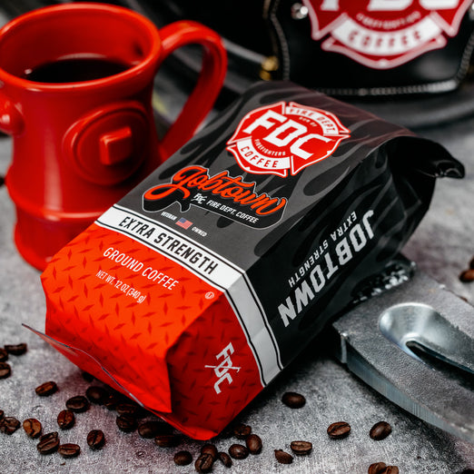 A 12 oz bag of Fire Department Coffee’s Jobtown Extra Strength Coffee surrounded by firefighter tools and an FDC Hydrant Mug.