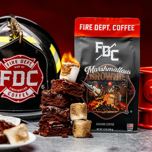 A bag of Fire Department Coffee’s 12 oz Marshmallow Brownie Coffee set on a table with a pile of brownies and toasted marshmallows next to it.