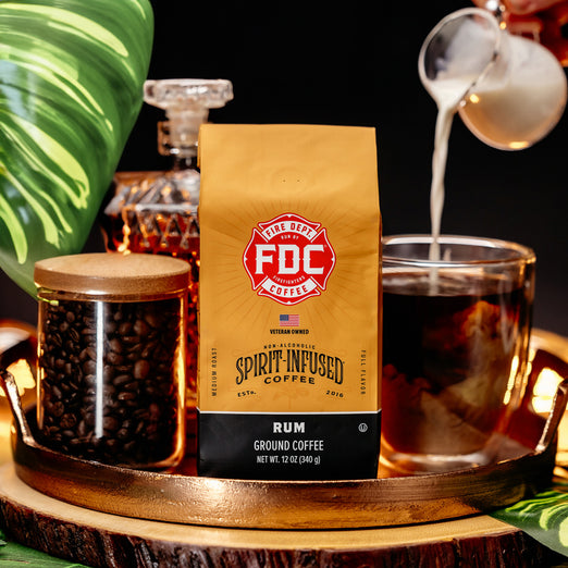 Fire Dept. Coffee’s 12 ounce Rum Infused Coffee on a tray surrounded by a brewed cup of coffee with milk and tropical plant leaves.