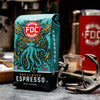 A 12-ounce package of Fire Department Coffee's Shellback Espresso Roast on a table with a red FDC tumbler and a small anchor.