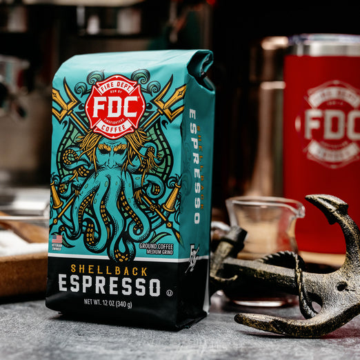 A 12-ounce package of Fire Department Coffee’s Shellback Espresso Roast on a table with a red FDC tumbler and a small anchor.