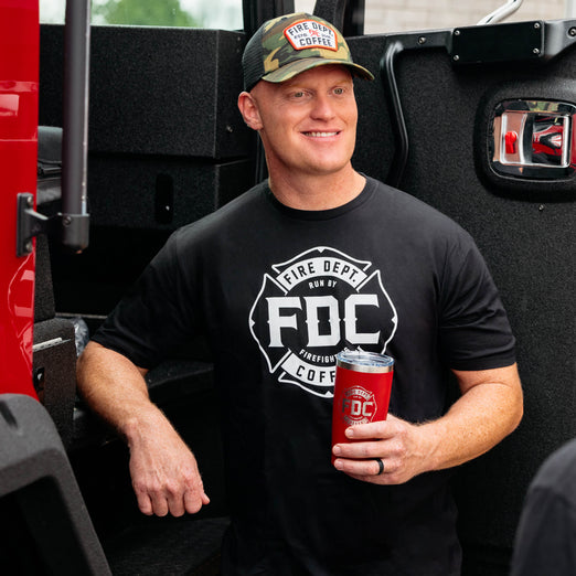 A man wearing the Fire Department Coffee Black Shirt and a Camo Keystone Hat with a Red FDC Tumbler.