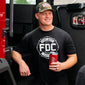 A man wearing the Fire Department Coffee Black Shirt and a Camo Keystone Hat with a Red FDC Tumbler.