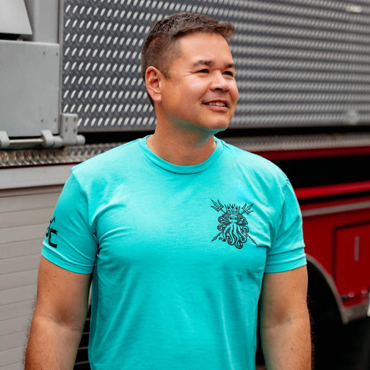 A man standing in front of a fire truck wearing the Shellback Shirt.