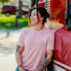 A woman wearing the Pink Stay Back Shirt resting against a fire truck.