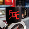Black mug sitting on the front of a fire engine with red FDC pike pole logo on the front and red inside of the mug